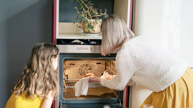 Young girl helping her mom take a finished baked treat out of the oven for Thanksgiving.
